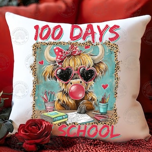 May include: White cushion featuring a cartoon Highland cow with heart-shaped sunglasses and a bubble. The text "100 DAYS SCHOOL" is displayed in red and teal. The design includes pencils and books.
