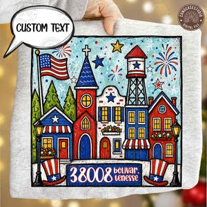 May include: A light gray sweatshirt featuring a colorful illustration of a town with an American flag, fireworks, and buildings in red, white, and blue. The text "CUSTOM TEXT" is in a speech bubble. The town's address is "38008 bolivar tenesse".