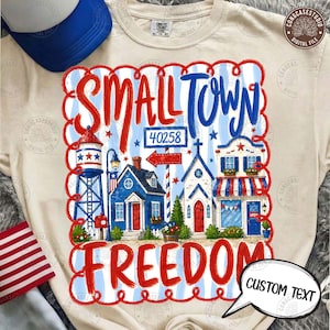 Könnte beinhalten: Ein cremefarbenes T-Shirt mit einem patriotischen Design. Die Grafik zeigt die Worte "SMALL TOWN FREEDOM" in Rot und Blau, zusammen mit Illustrationen eines Wasserturms, Häusern und einer Kirche sowie die Postleitzahl 40258. Eine Sprechblase sagt "CUSTOM TEXT".