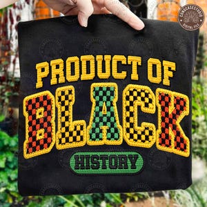May include: Black sweatshirt featuring the text "PRODUCT OF BLACK HISTORY" in yellow, green, and red checkered lettering. The sweatshirt is held up by a hand.