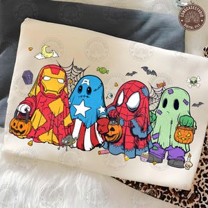 May include: A cream-colored sweatshirt featuring a graphic print of four characters dressed as ghosts for Halloween. The characters resemble Iron Man, Captain America, Spider-Man, and a green monster, each holding a jack-o'-lantern candy bucket.