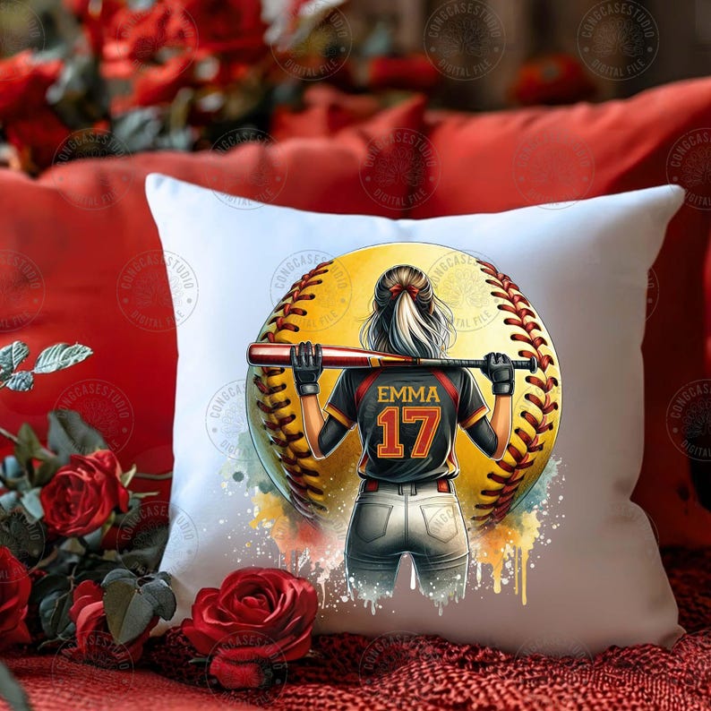 Peut inclure: Un oreiller blanc avec un motif aquarelle d'une joueuse de softball portant un maillot noir et rouge avec le num&eacute;ro 17 et le nom "Emma" au dos. La joueuse est debout devant une grosse balle de softball.