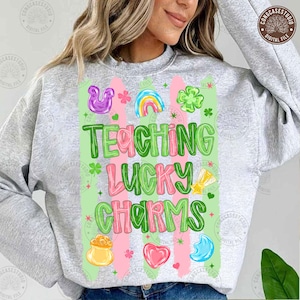 May include: A light gray sweatshirt with the words "TEACHING LUCKY CHARMS" in green and pink, surrounded by St. Patrick's Day themed graphics. The design includes a rainbow, shamrocks, and a pot of gold.