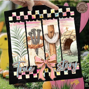 May include: Black t-shirt with a colorful Easter-themed design. The design includes a cross, nails, a crown of thorns, and the text "True Story" in a script font. A pink bow is also featured.