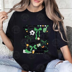 Puede incluir: Camiseta negra con un dise&ntilde;o tem&aacute;tico de f&uacute;tbol. El dise&ntilde;o incluye un bal&oacute;n de f&uacute;tbol, lazos verdes, un trofeo, una bota de f&uacute;tbol y las frases "Let's Kick Some Grass", "My Heart Is On That Field" y "One Shot One Goal".