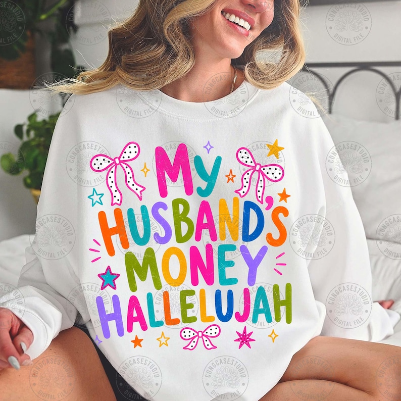 K&ouml;nnte beinhalten: Ein wei&szlig;es Sweatshirt mit Rundhalsausschnitt und dem bunten Schriftzug My HUSBAND'S MONEY HALLELUJAH in einer verspielten Schriftart. Das Design ist mit verschiedenen kleinen Sternen und drei gepunkteten Schleifen in Pink und Schwarz verziert.