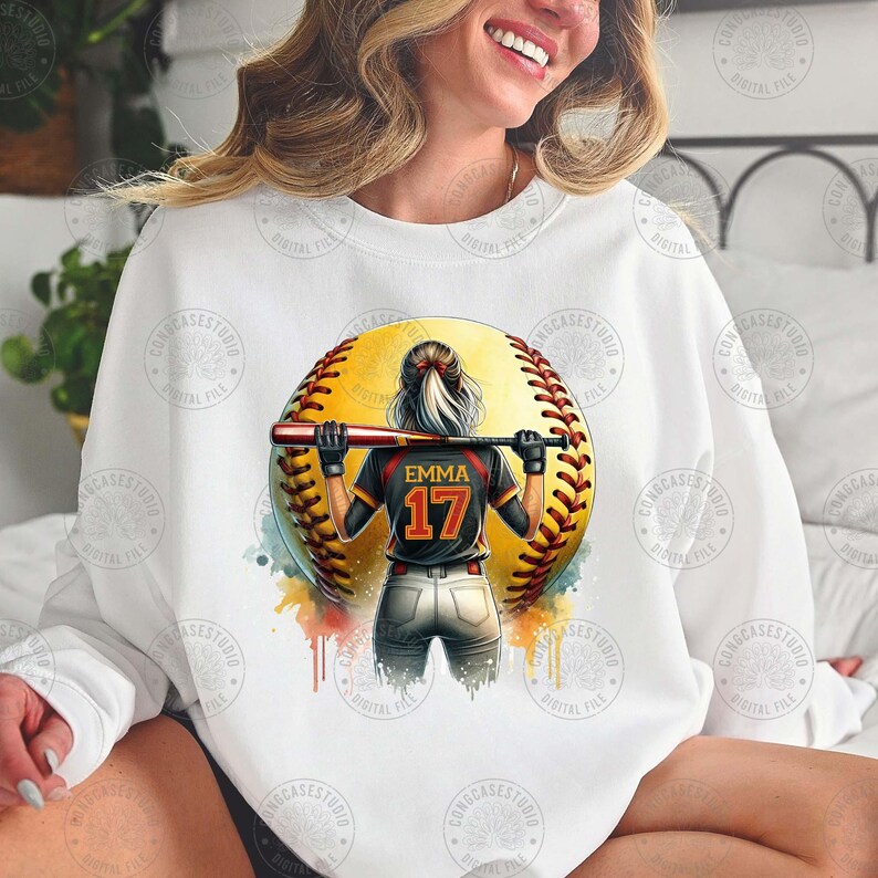 Peut inclure: Sweat-shirt blanc avec un motif aquarelle d'une joueuse de softball avec le texte "Emma 17" au dos de son maillot.