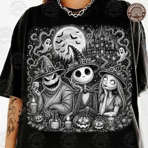 May include: A black t-shirt featuring a detailed white graphic print of three characters wearing witch hats, including a skeleton and a stitched creature. The scene includes a full moon, a haunted castle, ghosts, and pumpkins in a dark, stippled art style.