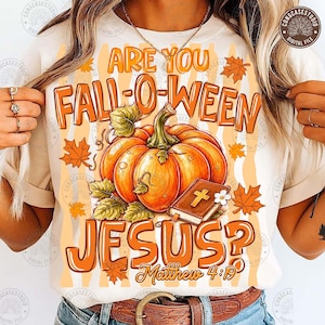 May include: A cream-colored t-shirt featuring a graphic print with the text ARE YOU FALL-O-WEEN JESUS? and Matthew 4:19. The design includes a large orange pumpkin, green leaves, scattered orange maple leaves, and a brown book with a gold cross.