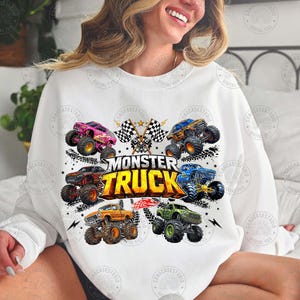 Puede incluir: Sudadera blanca con un gr&aacute;fico colorido de monster trucks. El dise&ntilde;o incluye varios monster trucks de diferentes colores, banderas a cuadros y el texto "MONSTER TRUCK".