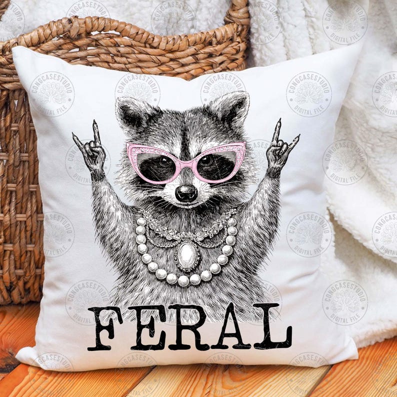 May include: White throw pillow with a black and white illustration of a raccoon wearing pink sunglasses and a pearl necklace. The raccoon is making a rock and roll hand gesture. The word "FERAL" is printed in black below the raccoon.