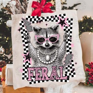 May include: A canvas tote bag featuring a raccoon wearing pink sunglasses and a pearl necklace. The raccoon is giving a rock and roll hand gesture. The word "FERAL" is printed in pink block letters below the raccoon.