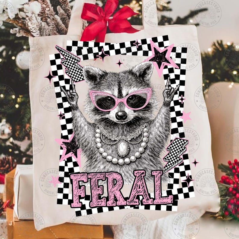 May include: A canvas tote bag featuring a raccoon wearing pink sunglasses and a pearl necklace. The raccoon is giving a rock and roll hand gesture. The word "FERAL" is printed in pink block letters below the raccoon.