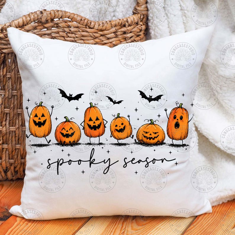 May include: A white square throw pillow featuring a graphic print of six orange jack-o'-lanterns with various facial expressions and thin black limbs. The design includes small black bats and stars, with the text "spooky season" in black script.