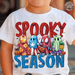 May include: A white t-shirt featuring the text SPOOKY SEASON in red and blue letters. The design includes four cartoon characters dressed as ghosts for Halloween, resembling Iron Man, Captain America, Spider-Man, and a green ghost with pumpkins.