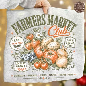 May include: A light gray heathered t-shirt featuring a graphic print with the text Farmers Market Club, Fresh From The Farm, Farm Fresh, and Locally Grown. The illustration depicts strawberries, blueberries, cherries, potatoes, tomatoes, and onions.