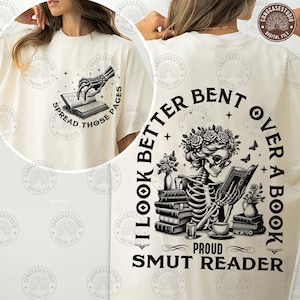 May include: A white t-shirt with a black and white graphic of a skeleton reading a book. The text on the shirt reads "I look better bent over a book, proud smut reader".