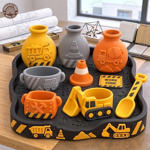 May include: A construction-themed desk organizer set featuring a black tray with yellow hazard stripes, two round vases with dump truck and cement mixer reliefs, a gray bowl, a traffic cone, a tool-themed cup, an excavator cup, and a shovel.