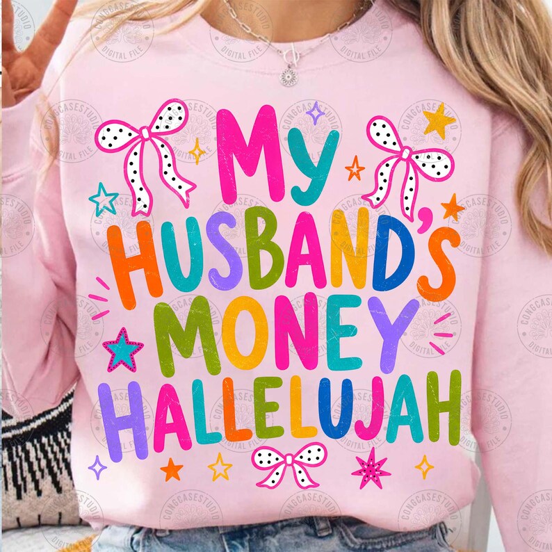 K&ouml;nnte beinhalten: Ein hellrosa Sweatshirt mit dem bunten Schriftzug "MY HUSBAND'S MONEY HALLELUJAH" in einer verspielten, mehrfarbigen Schriftart. Das Design ist mit wei&szlig;en gepunkteten Schleifen und verschiedenen kleinen, leuchtenden Sternen verziert.