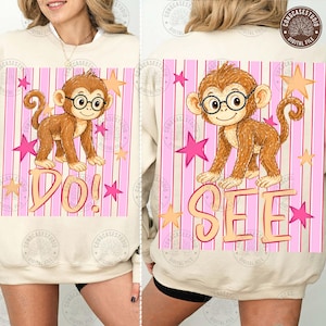 May include: Beige sweatshirt featuring a cartoon monkey wearing glasses, set against a pink striped background with stars. The word "DO!" is below the monkey on the front, and "SEE" on the back. A fun, playful design.