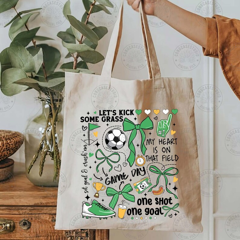 Puede incluir: Una bolsa de mano beige con un dise&ntilde;o tem&aacute;tico de f&uacute;tbol. El gr&aacute;fico incluye un bal&oacute;n de f&uacute;tbol, lazos verdes, una bota de f&uacute;tbol y texto que dice "Let's Kick Some Grass", "Game Day" y "My Heart Is On That Field."