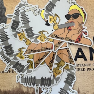 May include: A set of white stickers with a cartoon illustration of a woman wearing sunglasses and a red and white polka dot dress. The woman is holding a fuse in her mouth. The text "Blown Fuse" is written on the stickers.