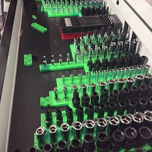 May include: A drawer filled with various sockets and tools, neatly organized on green holders. The sockets are black and silver, arranged in rows. The tools are in a white drawer.