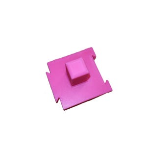May include: A bright pink 3D-printed object with a square base and a raised square in the center. The base has cutouts on each side. The object is set against a white background.