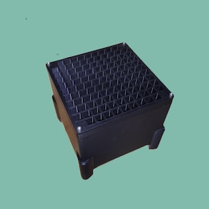 May include: A black, square organizer with a grid-like top and four supporting legs. The organizer is made of a solid, dark material and is designed to hold small items. The background is a solid, muted green.