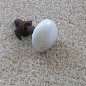 May include: A white ceramic door knob with a rusty metal stem and mounting bracket.