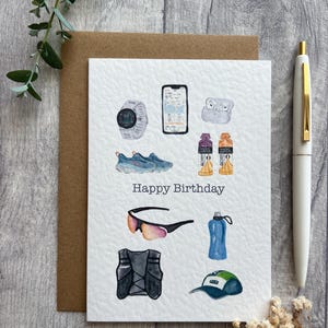 May include: Watercolor illustration of running-themed items on a white card with a brown envelope. The card features a watch, phone, shoes, sunglasses, vest, water bottle, hat, and the words "Happy Birthday."