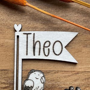 May include: Wooden sign with a heart at the top and a flag that says "Theo".