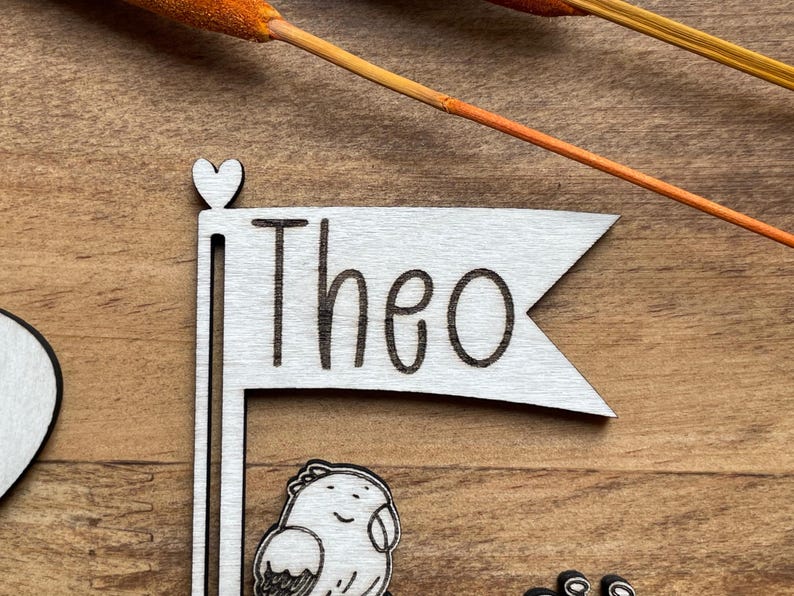 May include: Wooden sign with a heart at the top and a flag that says "Theo".