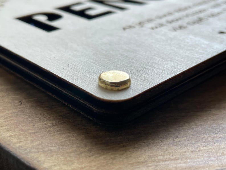 May include: Close-up of a wooden sign with the word "PEN" in black lettering. The sign is attached to a wooden surface with a gold metal screw.