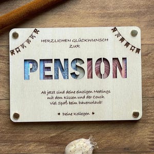 May include: A wooden sign with the text "HERZLICHEN GL&Uuml;CKWUNSCH ZUR PENSION" and a message about enjoying retirement. The sign is decorated with small flags.