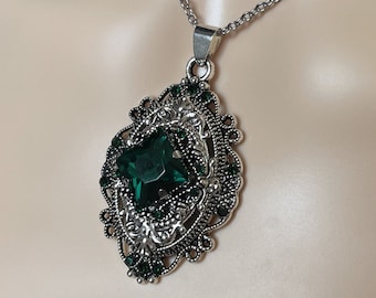 May include: A silver chain necklace with a green gemstone pendant. The pendant is ornate and features a filigree design.