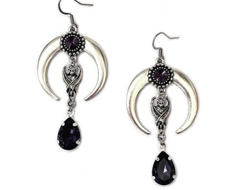 May include: Silver crescent moon earrings with a dangling teardrop-shaped purple crystal and a small bat charm.