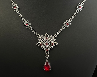 May include: A silver necklace with a red gemstone pendant. The pendant features a Celtic knot design with a teardrop-shaped gemstone hanging from the bottom.