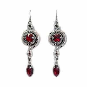 May include: Silver snake earrings with red crystal accents. The snake is coiled around a round red crystal and has a dangling red crystal drop.