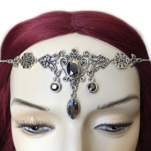 May include: Silver headband with a delicate chain and ornate design. It features a large, oval-shaped black gemstone in the center and smaller black gemstones hanging from the sides.