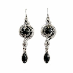 May include: Silver snake earrings with black crystal accents. The snake is coiled around a round black crystal and has a dangling black crystal drop.