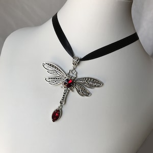 May include: A silver dragonfly pendant necklace with a red crystal body and black ribbon choker.