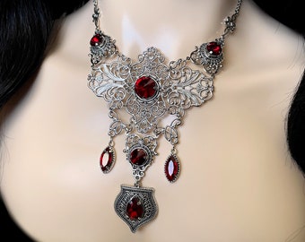 May include: A silver filigree necklace with a large, ornate pendant and multiple red gemstone accents.