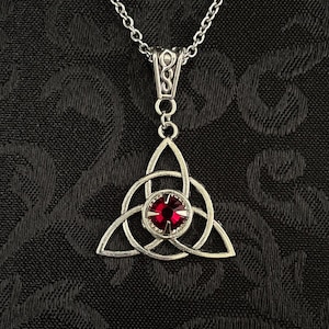 May include: Silver Celtic knot pendant necklace with a red gemstone in the center.