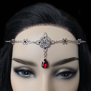 May include: Silver Celtic knot headpiece with a dangling teardrop-shaped red crystal. The headpiece is adorned with smaller red crystals.