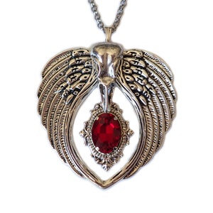 May include: A silver pendant necklace with a bird skull design and a large red gemstone. The pendant is shaped like a heart with wings.