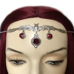 May include: Silver headband with a bat design and three dangling red crystals. The headband is adorned with a filigree pendant with a red crystal in the center.