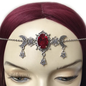 May include: Silver headband with a red gemstone and crescent moon accents. The headband is adorned with intricate filigree details.