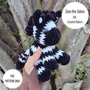 May include: A handmade crochet zebra plushie with black and white stripes. The plushie has a fluffy texture, blue eyes, and a round head. The image includes text that says "Zara the Zebra Pdf Crochet Pattern" and "PDF Pattern Only".