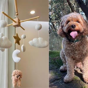 May include: A white, crocheted baby mobile with clouds, stars, and a crescent moon hanging from a wooden frame. A small, crocheted dog is hanging from the bottom of the mobile.